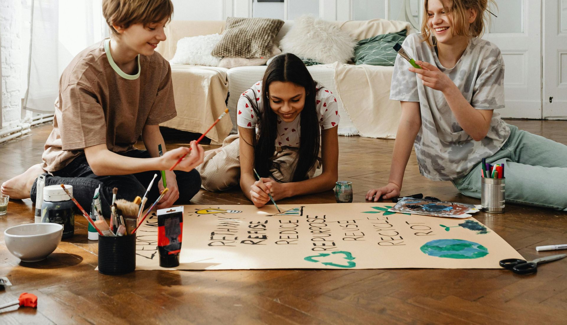 Three teenagers enjoy a fun art project together indoors, surrounded by paint and craft supplies.