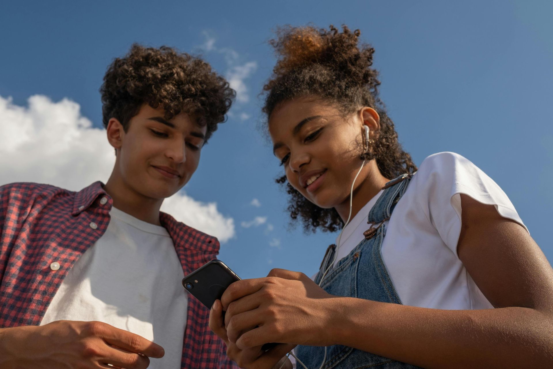 Two teenagers enjoy music together outdoors using a smartphone and earphones.
