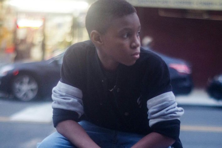A teenager in casual wear sits on a street railing, showcasing urban style.