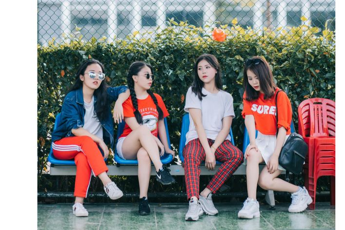 Stylish teen girls sitting outdoors in casual fashionwear, enjoying leisure time together.